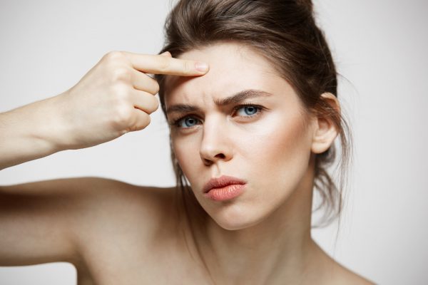 young brunette girl displeased her problem acne face skin white background health cosmetology skincare e1641197440743