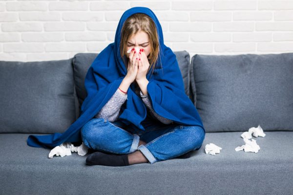 sick woman with rheum headache holding napkin sitting sofa with coverlet pills home e1642446429950